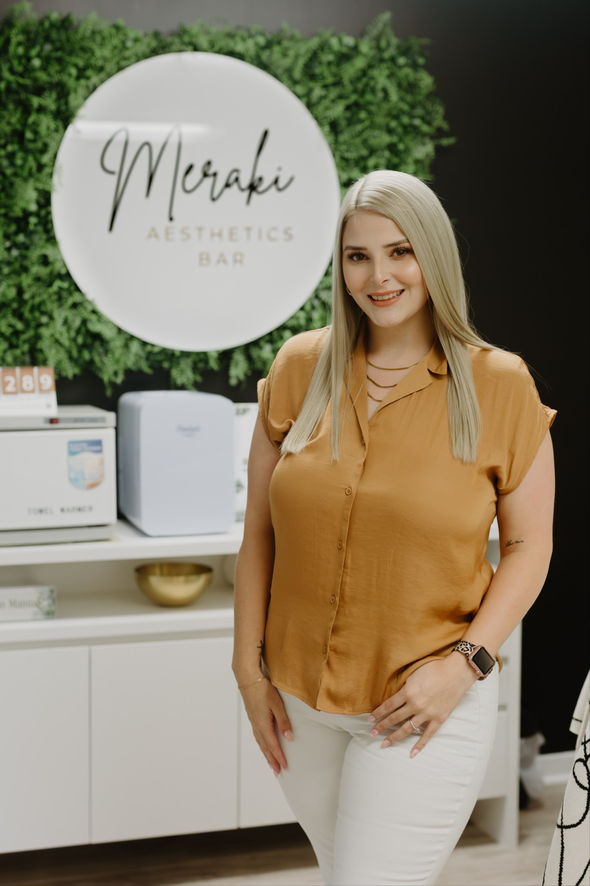 Standing in front of the Meraki Aesthetics Bar sign in the studio